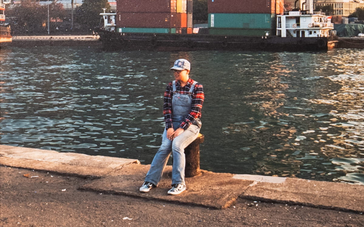 A man sits in front of a river in Hong Kong. This image is part of the 2024 installation Happy Valley by Pierfrancesco Celada.